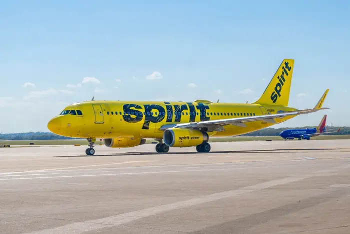Et gult Spirit Airlines-fly er parkert på en rullebane, med et annet fly synlig i bakgrunnen