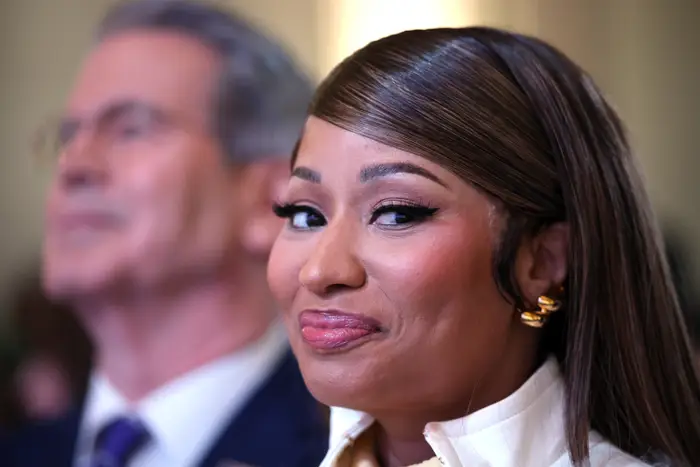 Nicki Minaj i elegant antrekk med stylet hår, iført bøyleøreringer, smiler subtilt mens han står ved siden av en passende person