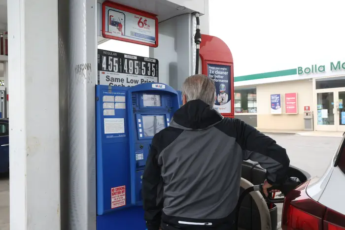 En person fyller drivstoff på bilen på en bensinstasjon og sjekker pumpeskjermen. Gassprisene er synlige på skiltet over