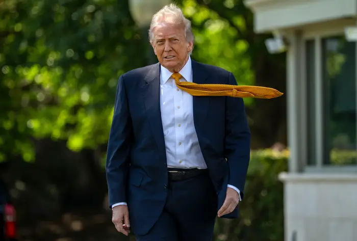 Donald Trump går utendørs med et slips som blåser dramatisk sidelengs i vinden