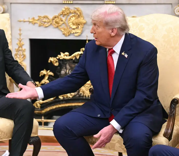 Donald Trump sitter, engasjert i samtale i det ovale kontor, og gestikulerer med hånden
