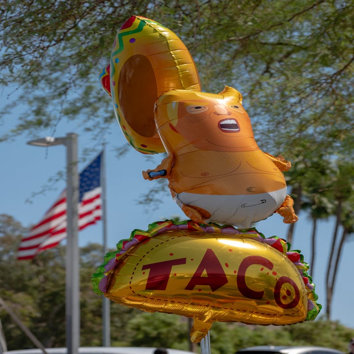 Oppblåst taco og taco-tema ballong, formet som en figur, med trær og et amerikansk flagg i bakgrunnen
