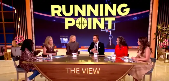 Seks paneldeltakere på et talkshow diskuterer et emne med et sportstema, indikert med 