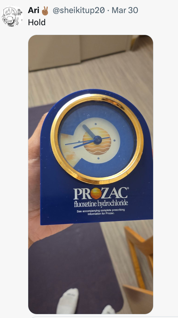 En hånd som holder en klokke som ligner en Prozac-pille, med merkenavnet og detaljene synlige