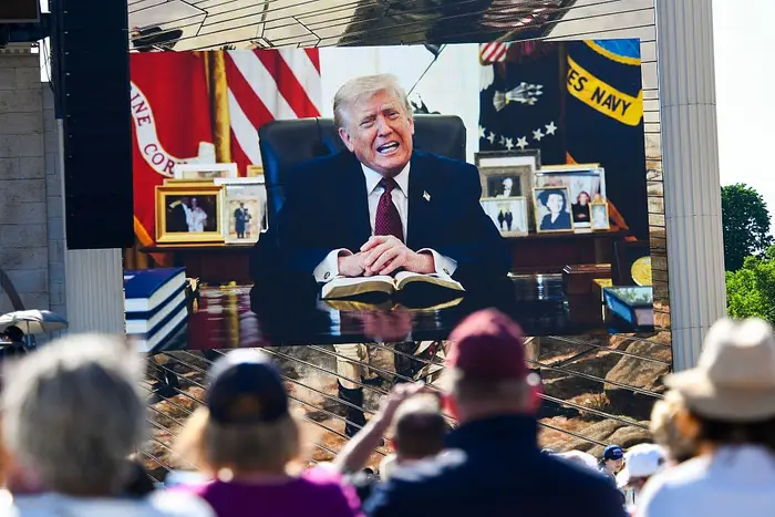 En folkemengde ser på en stor skjerm som viser Trump resitere et bibelsted i det ovale kontoret
