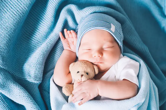 Baby sover fredelig, pakket inn i et teppe, holder en liten bamse