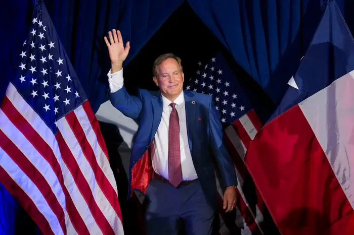 Person i dress vinker mens han står mellom amerikanske flagg på en scene