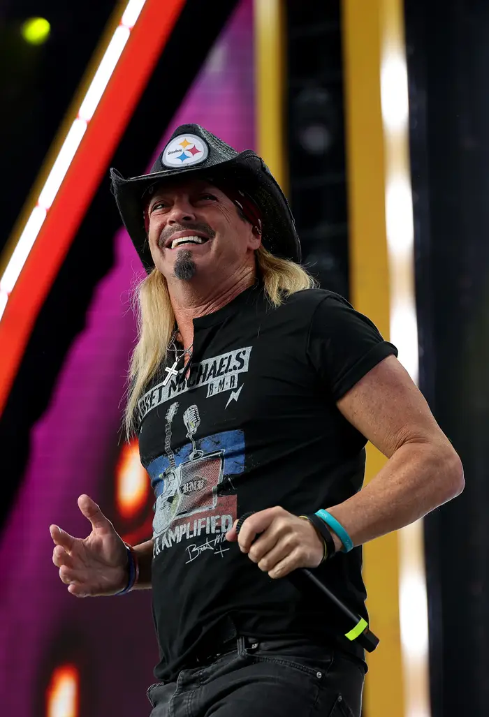 Musiker iført en grafisk T-skjorte og cowboyhatt, smilende på scenen under en forestilling