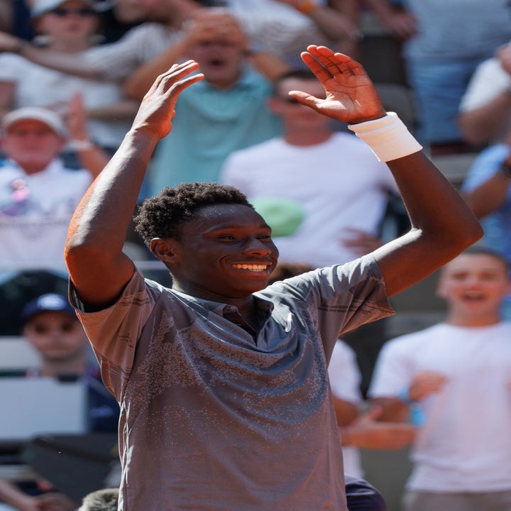 Tennisspiller smiler og løfter armene til seier på banen, med jublende publikum i bakgrunnen