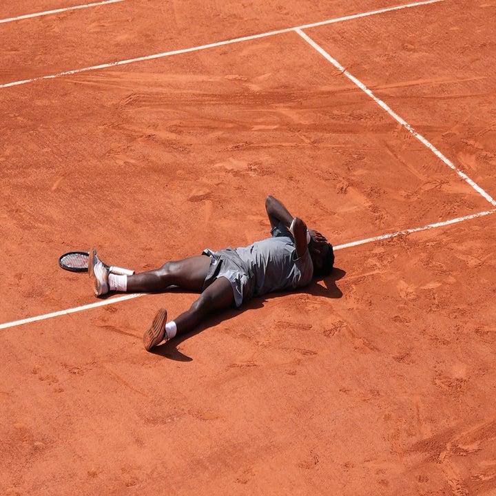 Tennisspiller liggende på en leirebane, synlig utmattet, med racketen i nærheten