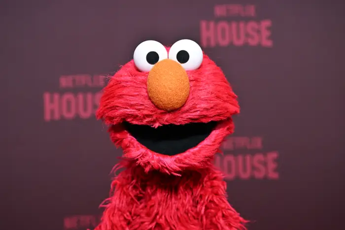 Elmo fra Sesame Street på et Netflix-arrangement, smilende med en vidåpen munn, stående mot et bakteppe med Netflix House-logoer