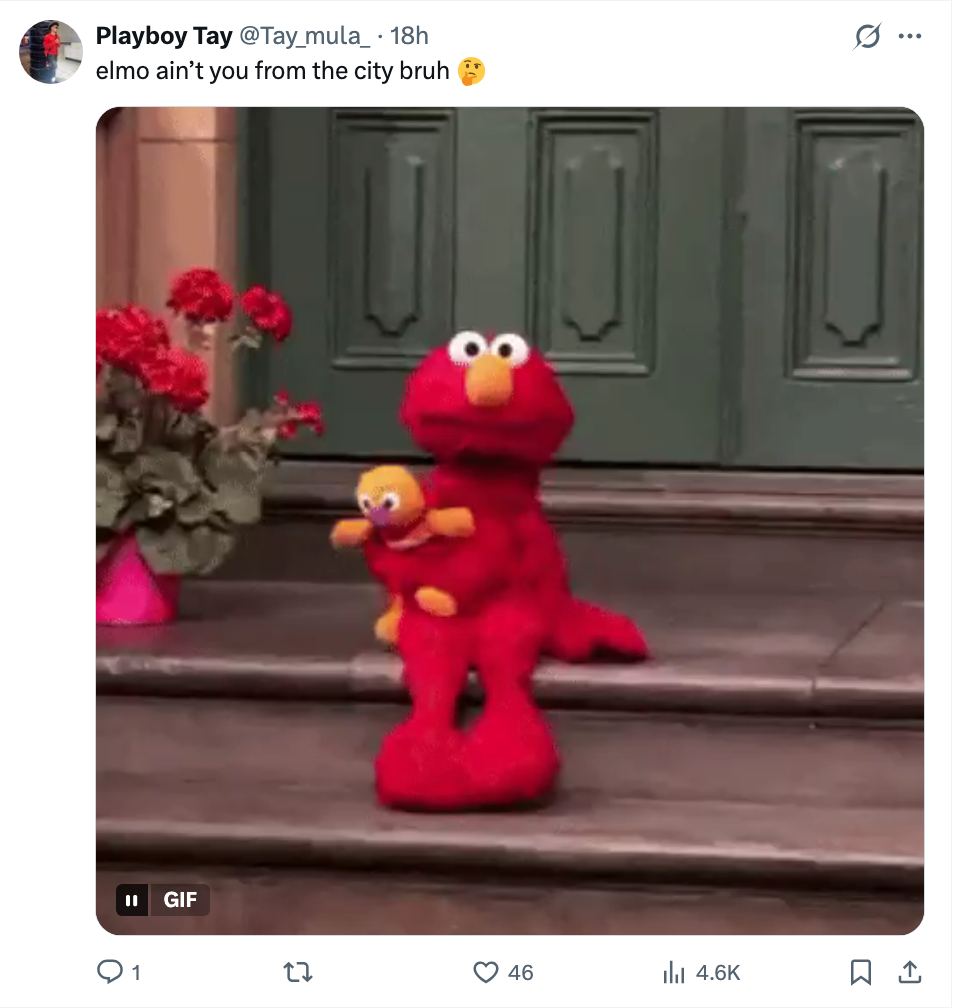 Elmo sitter på trapper og holder en liten dukke, med et lekent uttrykk. Tweet-tekst stiller humoristisk spørsmål ved Elmos byopprinnelse