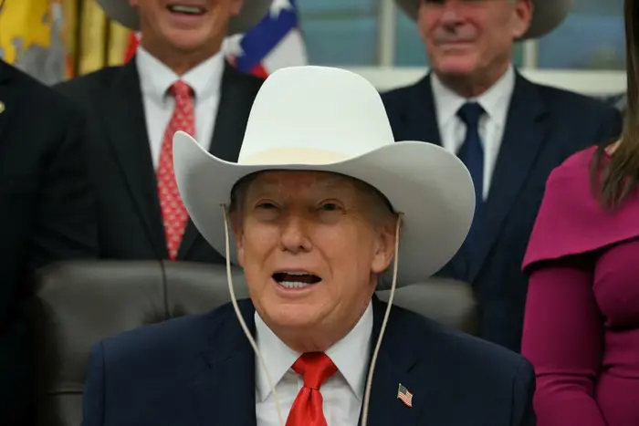En person i dress og cowboyhatt snakker mens andre i dress og hatt står bak dem