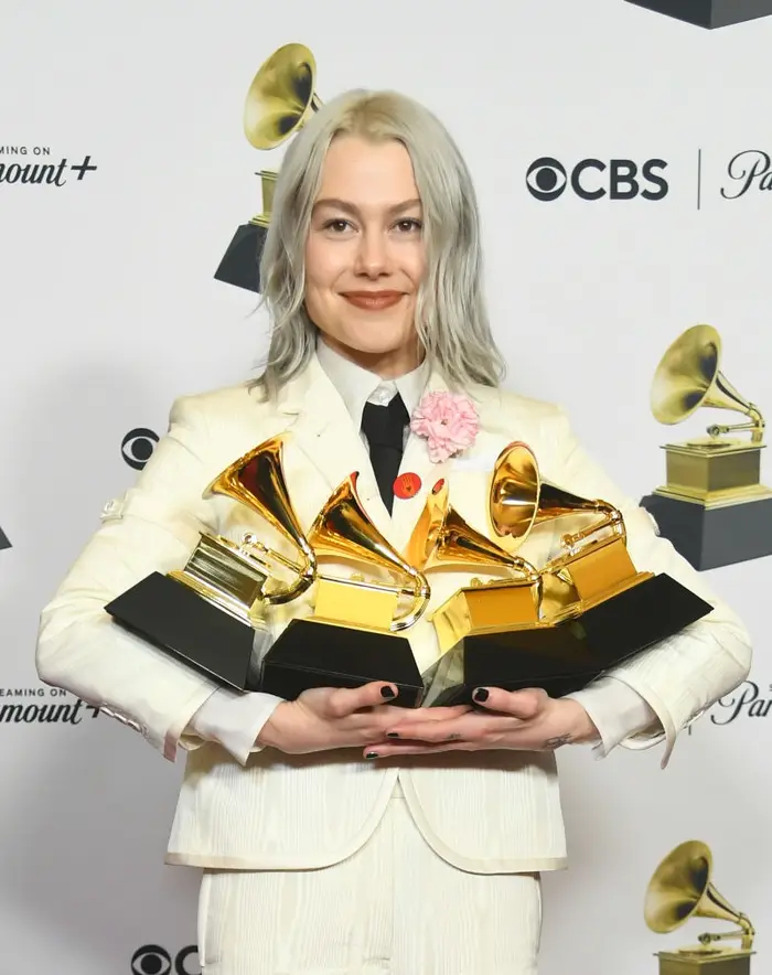 En person i hvit dress har flere Grammy-priser, smilende på den røde løperen med en blomsternål på jakkeslaget