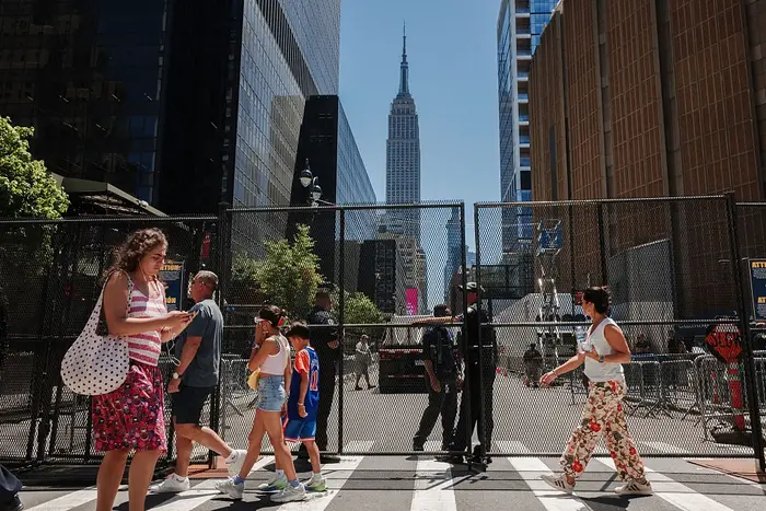 Folk som går i en bygate foran et inngjerdet område med Empire State Building synlig i bakgrunnen. Urbant kjas og mas