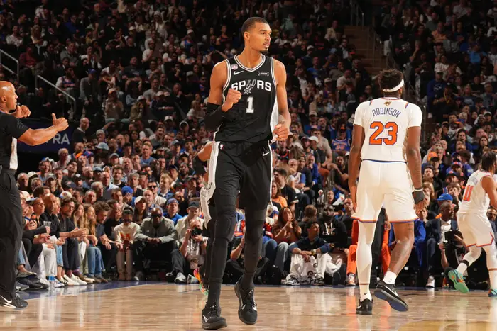Basketballspiller i Spurs-trøye nr. 1 på en bane, omgitt av spillere og et jublende publikum