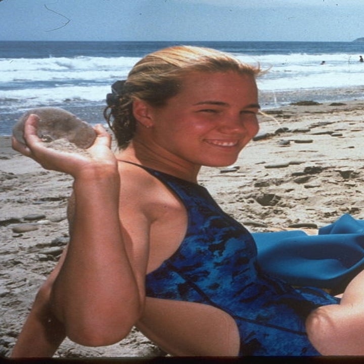 Person som slapper av på en strand med et lekent uttrykk, holder en rund gjenstand. Andre strandgjengere i bakgrunnen og bølger ved kysten