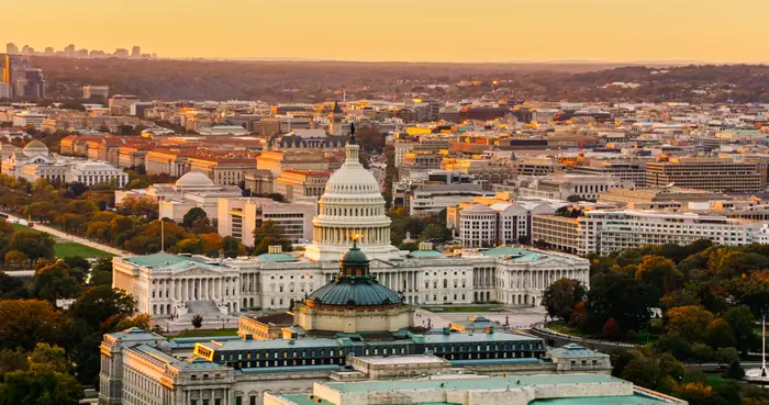 Luftfoto av US Capitol-bygningen i Washington, DC, med omkringliggende bybilde og fjerne åser under en gylden himmel