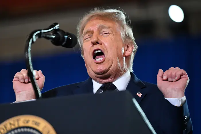 Donald Trump står på et podium med en mikrofon og snakker tullete med øynene lukket og hendene hevet