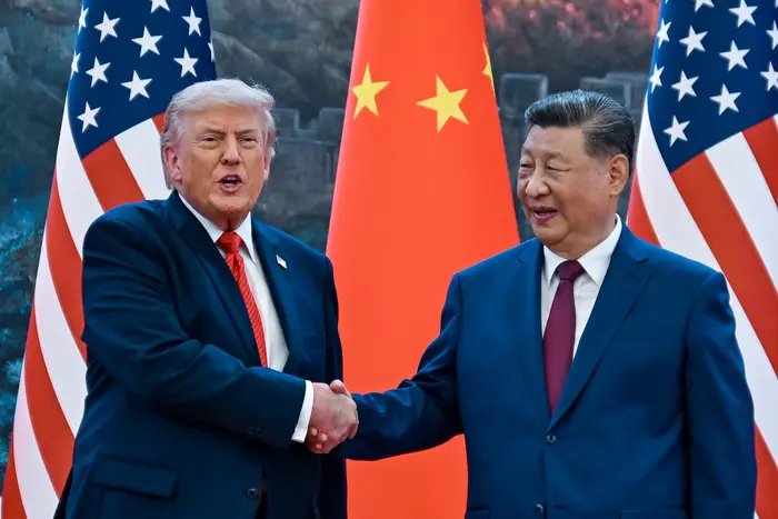 To personer i dress håndhilser foran amerikanske og kinesiske flagg, noe som tyder på et formelt diplomatisk møte