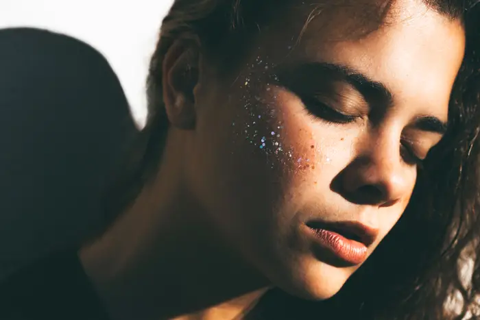 Person med lukkede øyne, avslappet uttrykk og glitter på kinnet. Omtalt i en helseartikkel