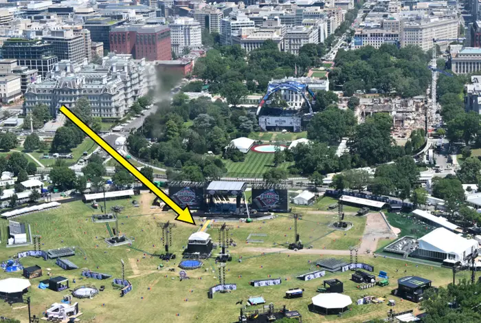 Luftfoto av et utendørs konsertoppsett i en bypark med scene, utstyr og omkringliggende bylandskap