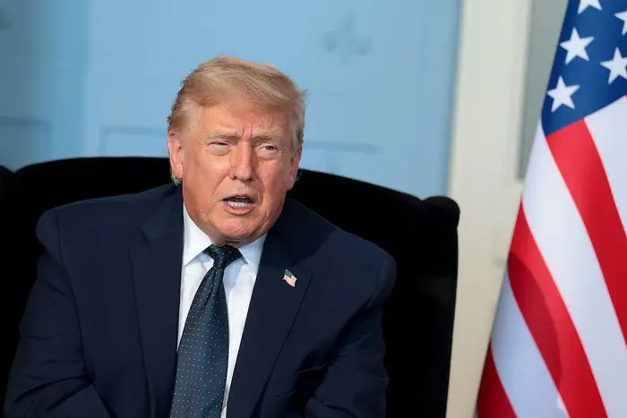 En person i dress snakker, som sitter ved siden av et amerikansk flagg