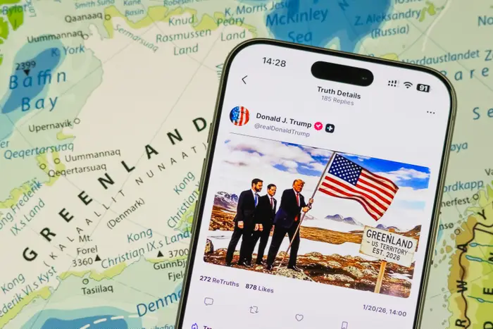 Smarttelefon som viser et innlegg på sosiale medier med en mann som holder et amerikansk flagg på Grønland. Bakgrunnskartet viser Grønlands plassering