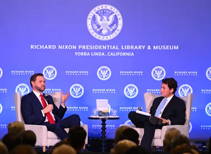 To personer satt på scenen på et diskusjonsarrangement, med et Richard Nixon Foundation-bakteppe