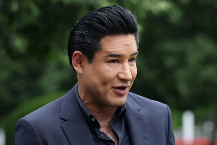 Mario Lopez i dress snakker utendørs og deler en engasjerende eller livlig kommentar