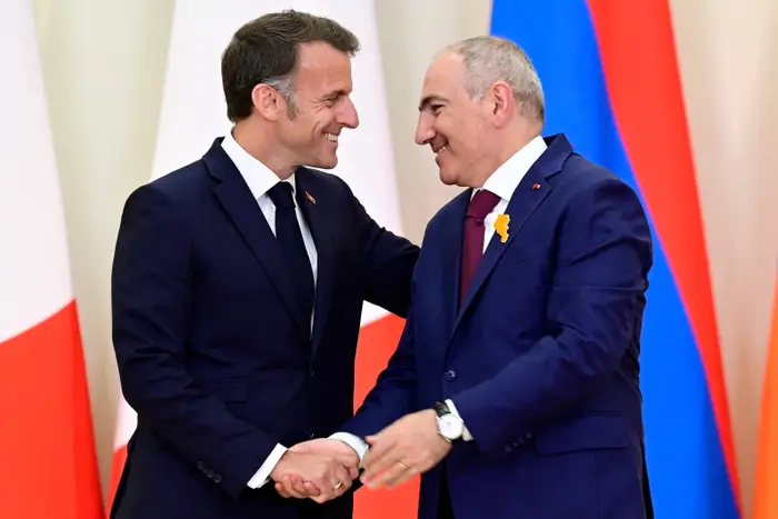 To menn i formelle dresser smiler og håndhilser på en diplomatisk begivenhet
