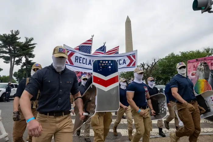 En gruppe maskerte individer i matchende antrekk marsjerer med skjold nær Washington-monumentet og holder 