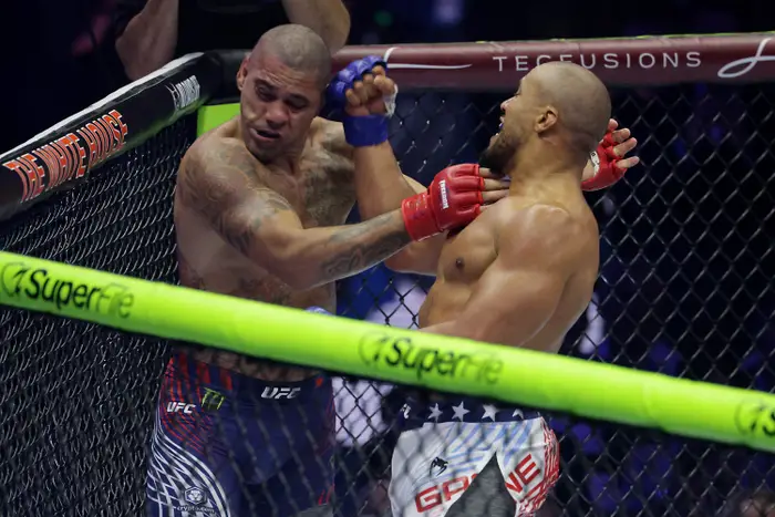 To UFC-krigere i en intens ringkamp. Den ene kaster et slag mens den andre blokkerer den mot bakteppet av buret