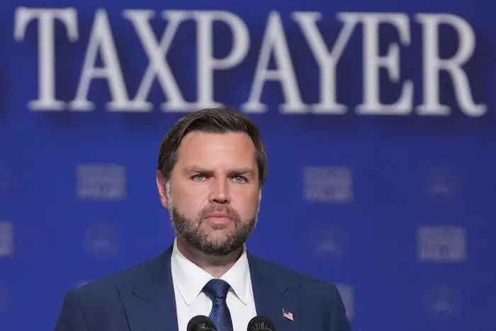 En mann i dress snakker foran et bakteppe med ordet «Skattebetaler».