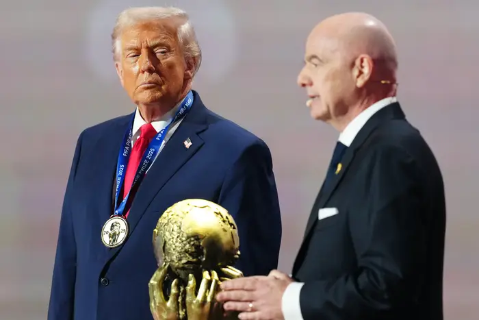 To menn står på scenen; den ene i dress med medalje og den andre taler og holder et klodeformet trofé