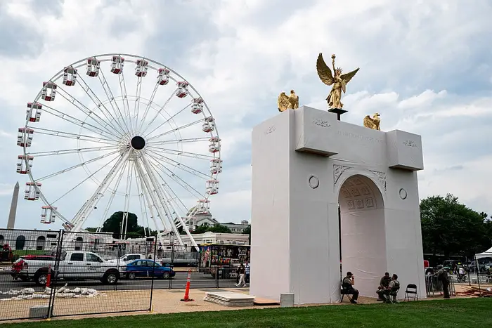 Pariserhjul ved siden av en stor buegang-replika med gylne statuer. Vakter sitter i nærheten. Travle parkomgivelser med biler og mennesker