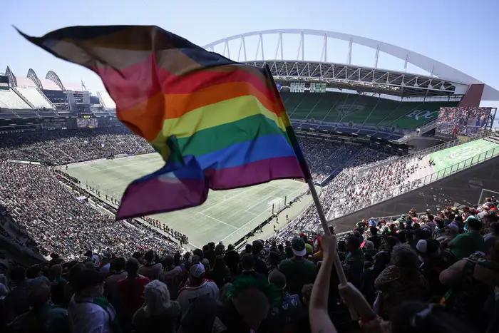 Et publikum ser på en fotballkamp på et stadion. En person vifter med et pride-flagg, som indikerer støtte for LHBTQ+-rettigheter