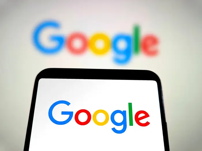 Telefon som viser Google-logo med en uskarp større Google-logo i bakgrunnen