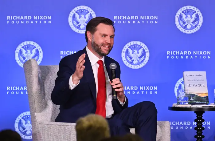 Person i dress som snakker på scenen ved et Richard Nixon Foundation-arrangement, med en bok med tittelen 