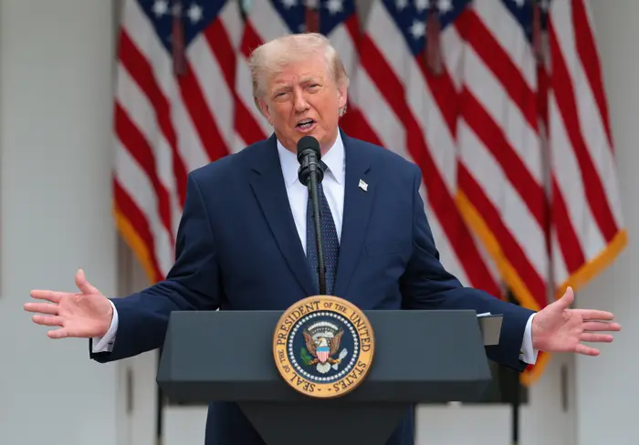 En person står på et podium med et presidentstempel og snakker til et publikum. Amerikanske flagg vises i bakgrunnen