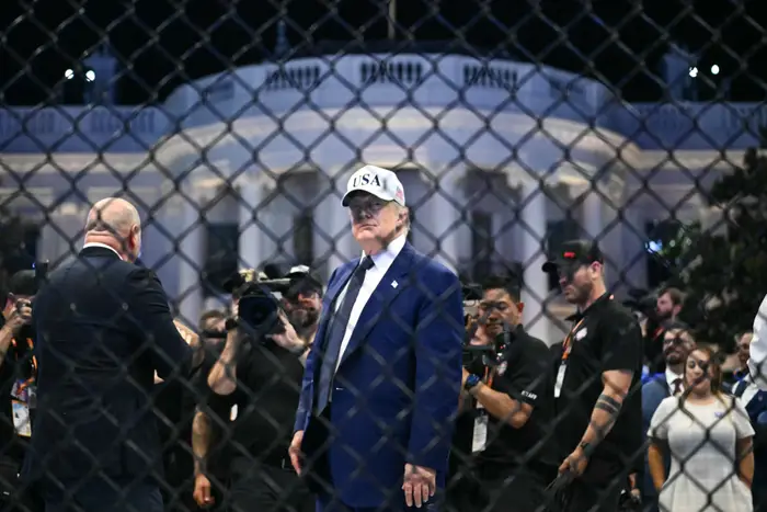 USAs president Donald Trump står inne i et bur, omgitt av fotografer og ansatte, med en kuppelformet bygning i bakgrunnen