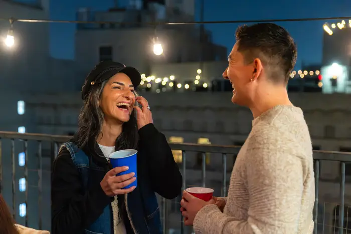 To personer som smiler og prater på et hustak om natten, begge holder drinker