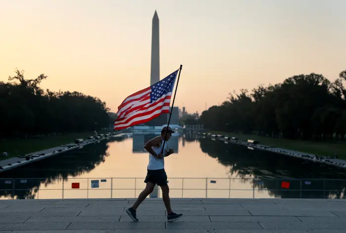 En person løper med et stort amerikansk flagg nær Reflecting Pool, Washington Monument i bakgrunnen, under soloppgang