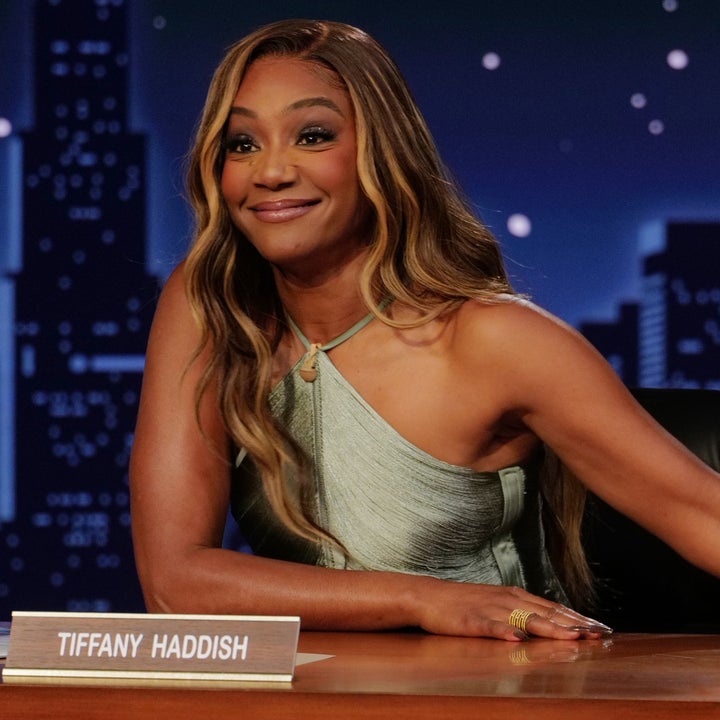 Tiffany Haddish sitter ved en talkshow-pult og smiler med en selvsikker positur. Har på seg et ermeløst, asymmetrisk antrekk