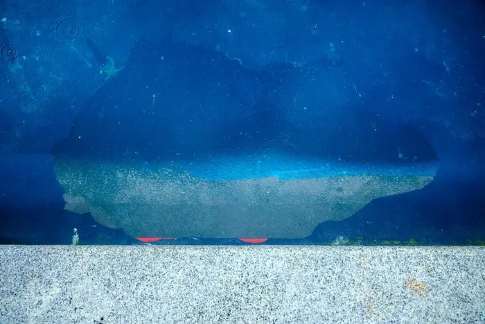 Våt betongoverflate med skateboard delvis nedsenket i en sølepytt, hjulene delvis synlige
