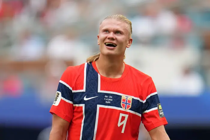 Person i sportsdrakt med norsk flaggdesign, smilende, dukker opp på en idrettsbane under et offentlig arrangement