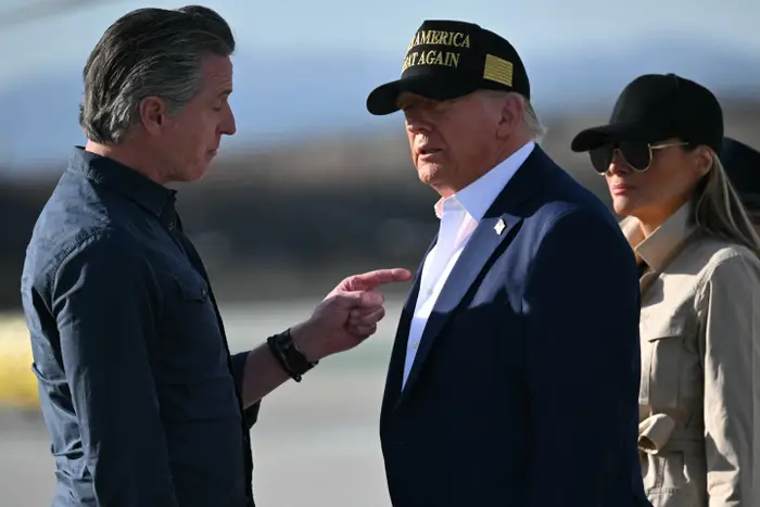 Person som gestikulerer mens han snakker med en annen person som har på seg en "Make America Great Again" cap, med en tredje person i solbriller i nærheten