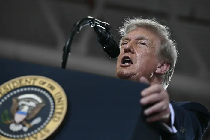 En mann taler ved et podium med presidentseglet, og taler til en folkemengde på et innendørsarrangement