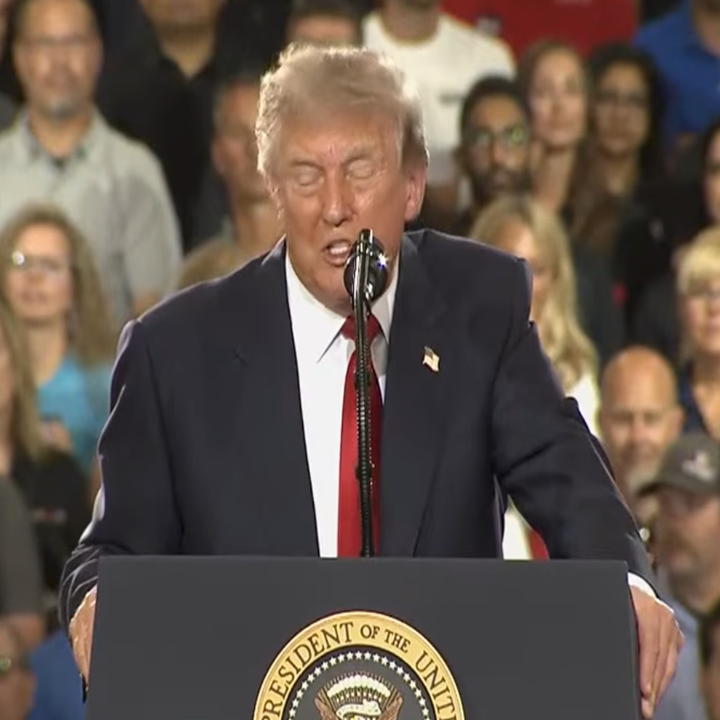 En offentlig person holder en tale på et podium med presidentens segl til en folkemengde