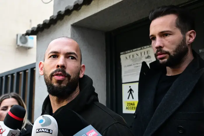 To personer blir intervjuet av media utenfor en bygning. Diverse mikrofoner i forgrunnen